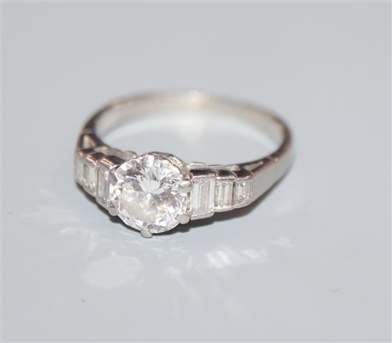 A white metal and single stone diamond ring, with graduated baguette cut diamond set shoulders, size K.